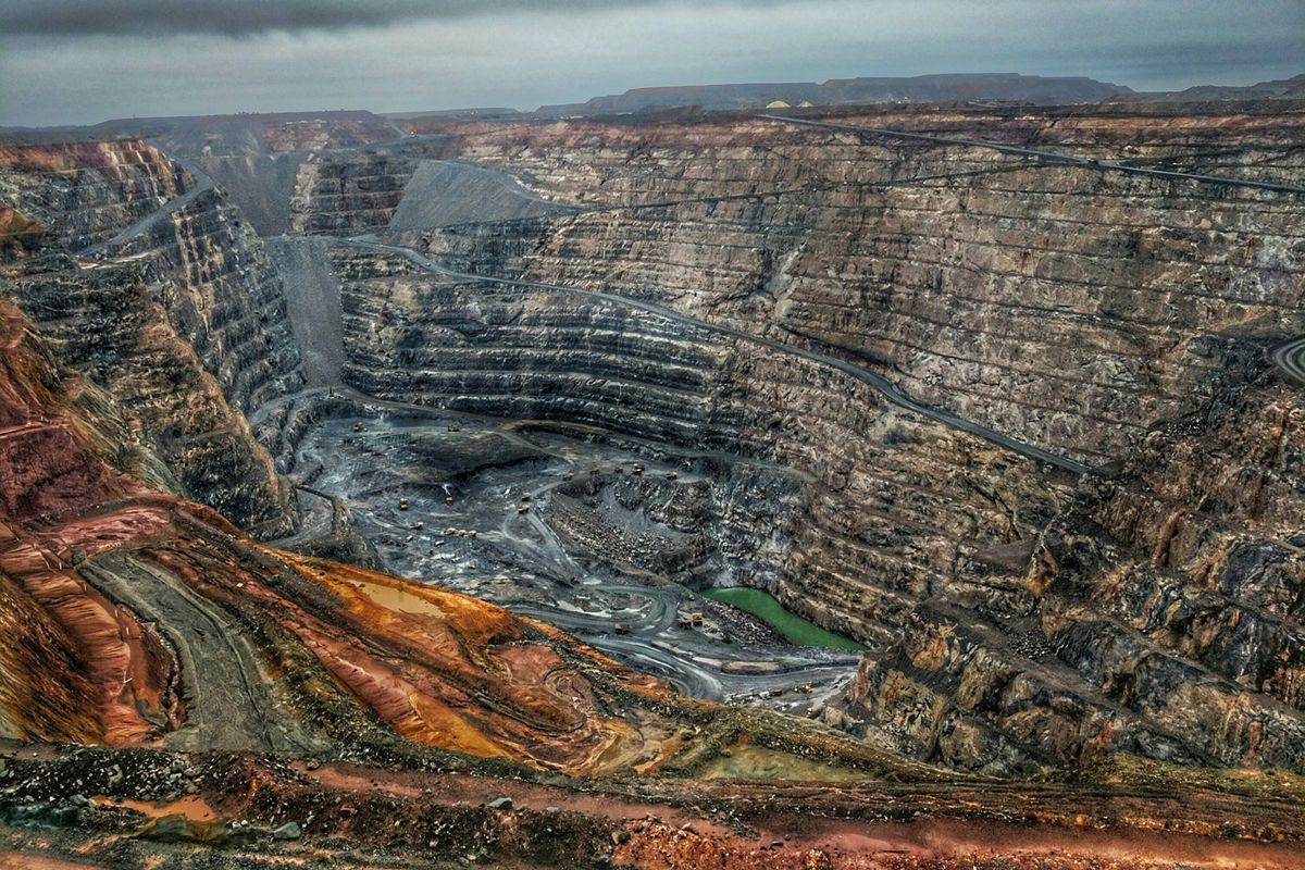A large open-pit mine with terraced benches and haul roads under a grey sky