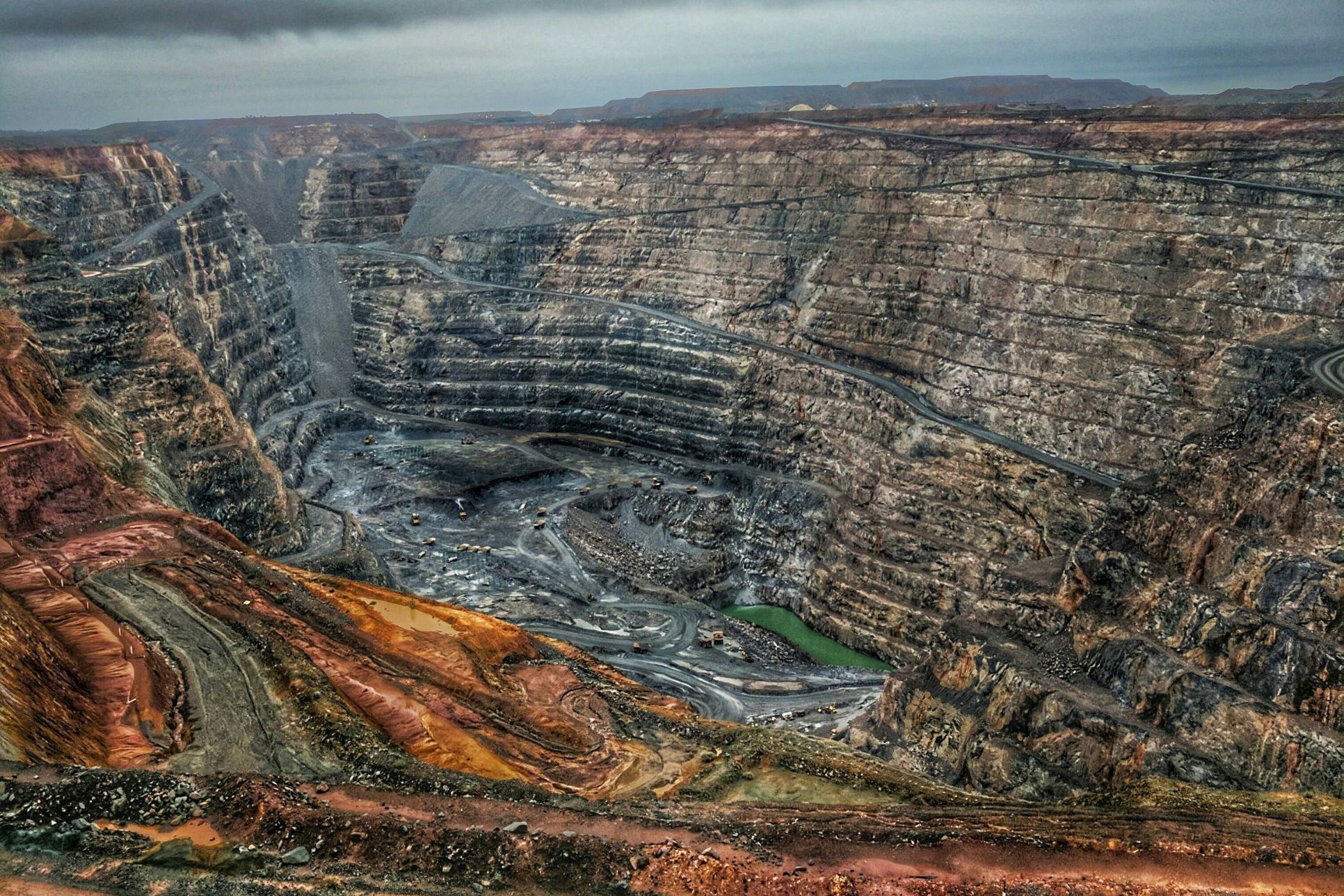 A large open-pit mine with terraced benches and haul roads under a grey sky