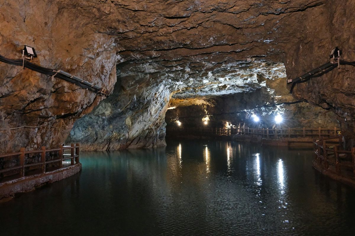 A flooded underground mine gallery lit by floodlights, with a walkway along the water